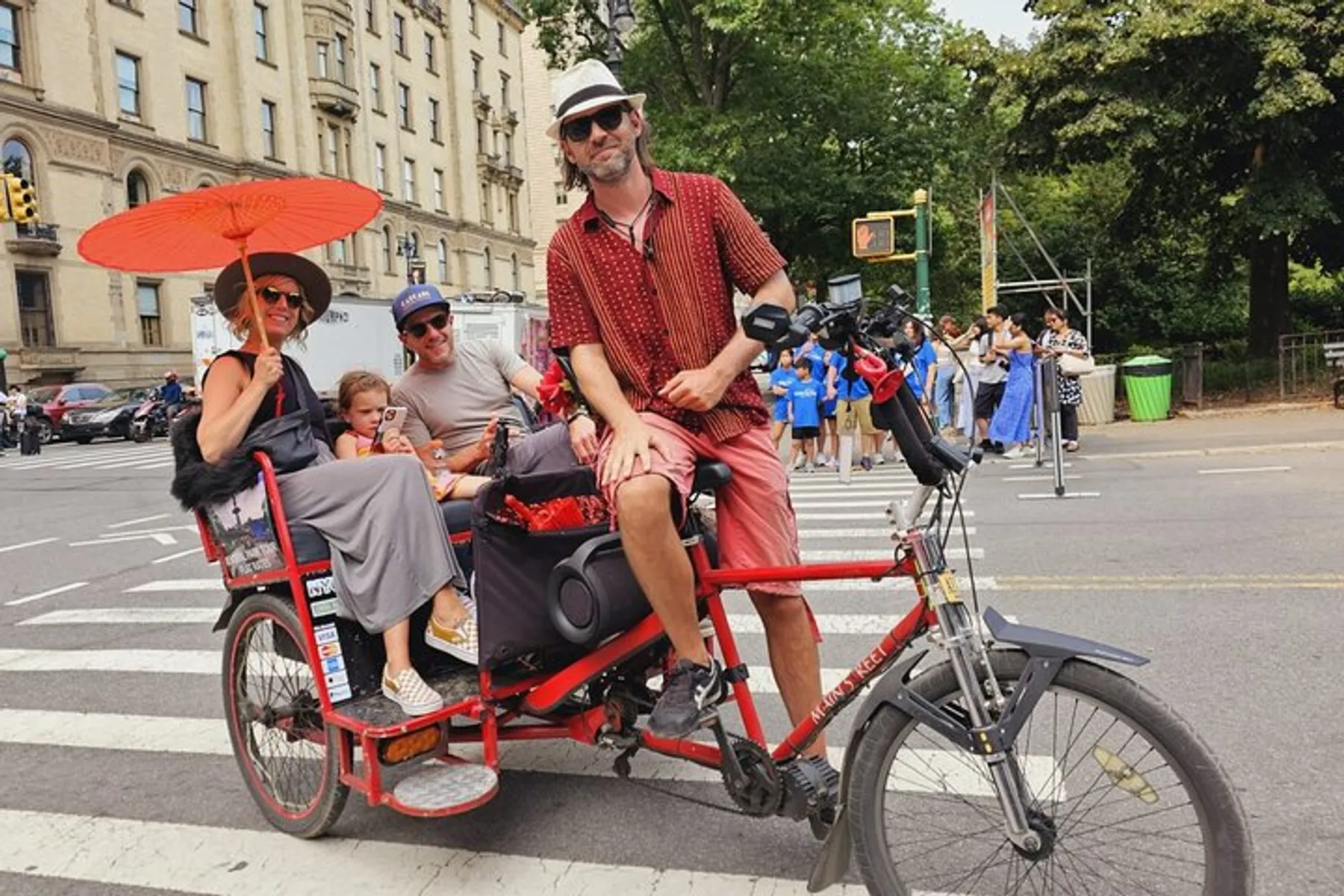 A family is enjoying a ride on an urban pedicab with the driver at the front and a woman holding a red parasol seated behind him.