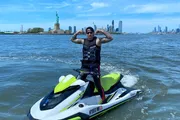 A person is posing on a jet ski in a body of water with the Statue of Liberty and the New York City skyline in the background.