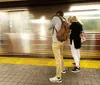 Two people stand on a subway platform as a blur of a train passing by is captured in the background