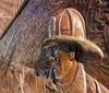 This image features a close-up view of a firefighters face in profile sculpted in relief on a bronze memorial wall with a blurred American flag flying in the background