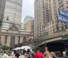 The image depicts a bustling city street corner with pedestrians diverse architecture including a historic building modern skyscrapers vehicles and street signs indicating East 41st Street and Library Way