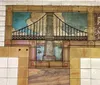 The image displays a mural of a bridge depicted in a stained glass art style on a tiled wall