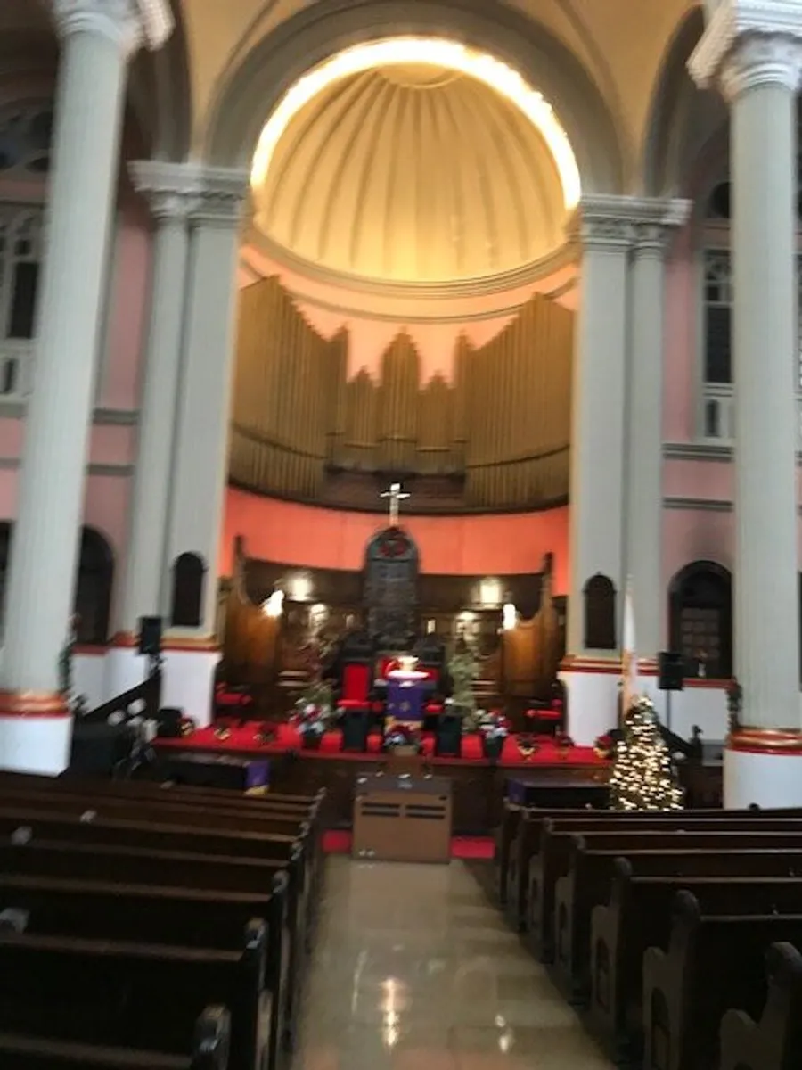 The image shows the interior of a church with rows of pews, a decorated Christmas tree, and a prominent organ at the back of the altar area, under a rounded ceiling.