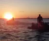 Two individuals are riding jet skis on a body of water at sunset with a city skyline visible in the background