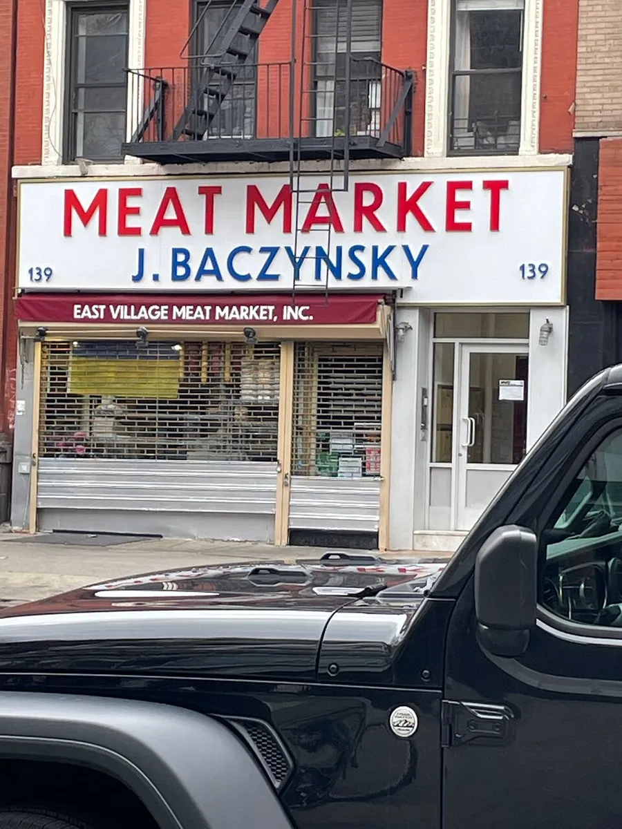 The image shows a storefront with a sign that reads MEAT MARKET J. BACZYNSKY above a closed security gate, indicating it may be a specialty butchery named after someone with Eastern European heritage, located at building number 139.