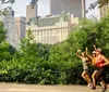 Three people are jogging in a park with a backdrop of skyscrapers and lush trees