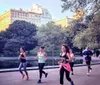 Three people are jogging in a park with a backdrop of skyscrapers and lush trees