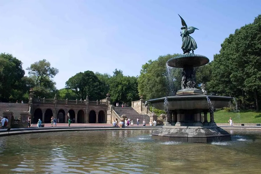 The image shows a tranquil scene at a large fountain with a statue on top, surrounded by water and set against a backdrop of steps and archways, with people leisurely enjoying the serene environment.