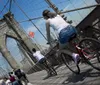 Cyclists and pedestrians share the pathway on the Brooklyn Bridge under a sunny sky