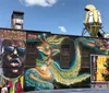 The image shows a vibrant street mural featuring colorful cartoonish snake characters on a buildings exterior with two people and a truck visible in front of the artwork
