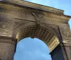 This image shows the intricately detailed Washington Square Arch in New York City lit by a soft glow against the evening sky