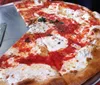 A large Margherita pizza with slices missing is displayed on a table with a pizza peel spatula on the side