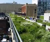 People are walking along a lush green urban park built on an elevated rail line above city streets