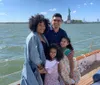 A happy family is posing for a photo on a boat with the Statue of Liberty in the background on a sunny day
