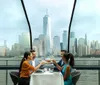 Four individuals are enjoying a meal at a dining table with a panoramic view of a city skyline in the background