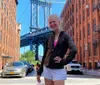 A smiling person is standing on a cobblestone street with the Manhattan Bridge in the background