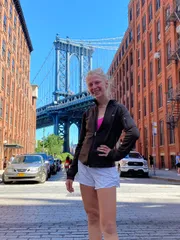 A smiling person is standing on a cobblestone street with the Manhattan Bridge in the background.