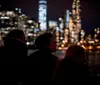 Three silhouetted individuals are gazing at a brightly lit city skyline at night across a body of water