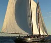 A group of people are enjoying a sail on a large traditional sailing yacht with its sails fully billowed in the late afternoon sun