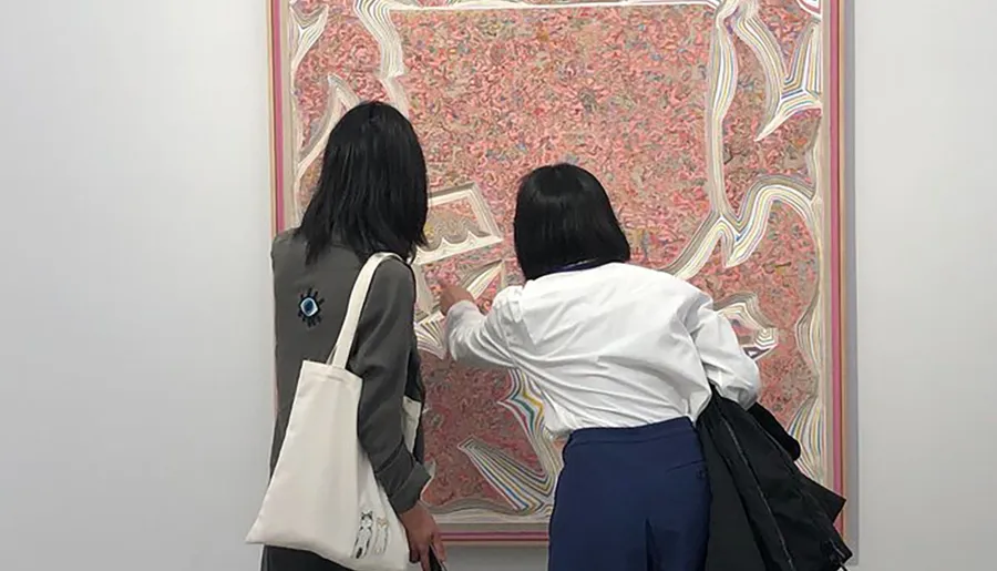 Two individuals are closely examining an intricately patterned artwork at a gallery.