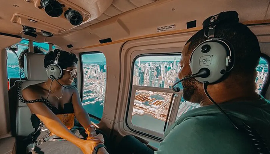 Two people are wearing headphones while enjoying a helicopter ride with a view of a city skyline.