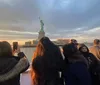 A group of people are capturing the view of the Statue of Liberty with their phones at sunset