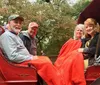 Four people are smiling for the camera while sitting in a red horse-drawn carriage covered with a red blanket and adorned with colorful artificial flowers