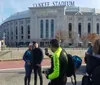 A person is taking a photo of two people with Yankee Stadium in the background