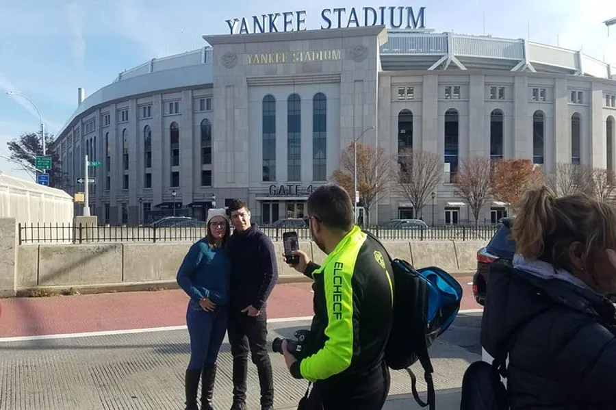 A person is taking a photo of two people with Yankee Stadium in the background.