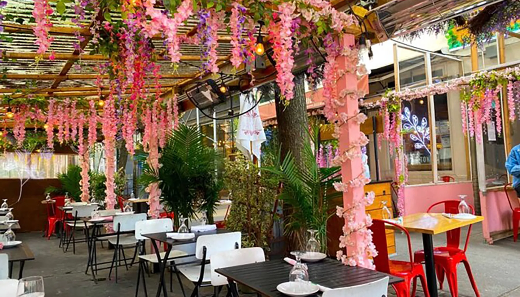 The image shows an outdoor restaurant patio adorned with pink artificial flowers, providing a colorful and inviting ambiance for dining.