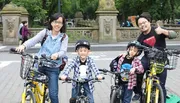 A family of four is posing for a photo with their bicycles in a park, smiling and appearing to be enjoying their day out together.