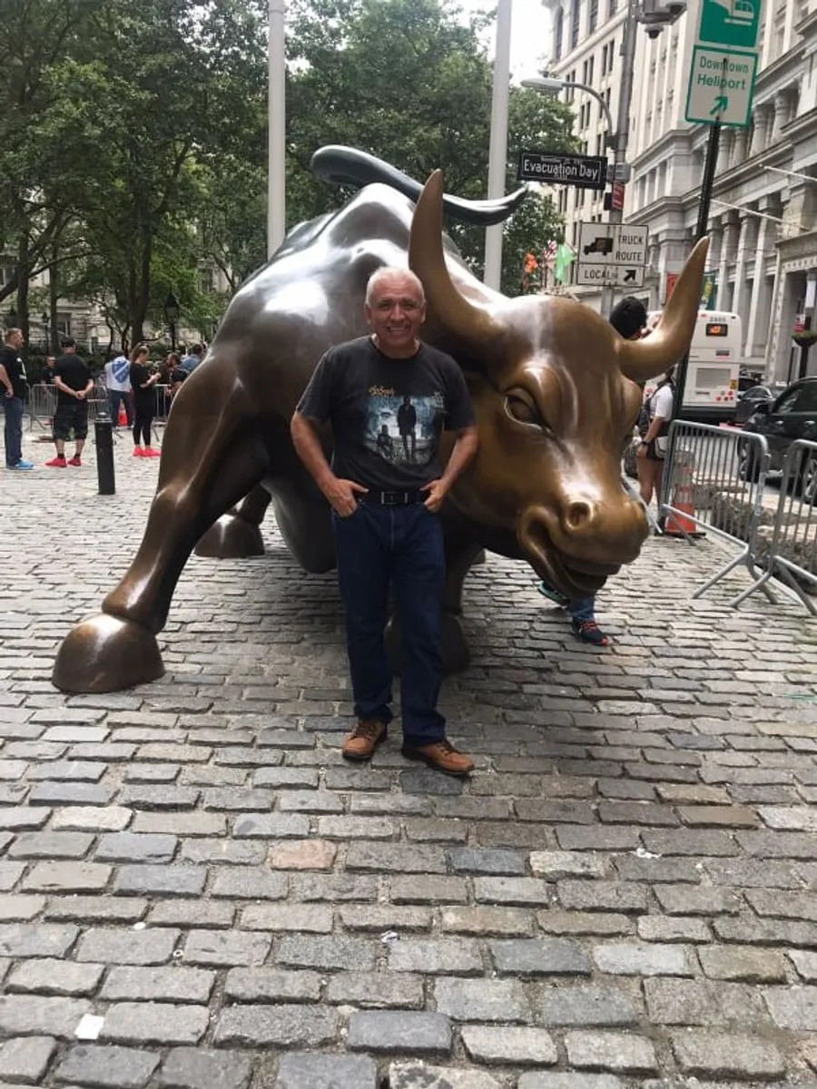 A man is standing in front of the Charging Bull statue in the financial district of New York City.