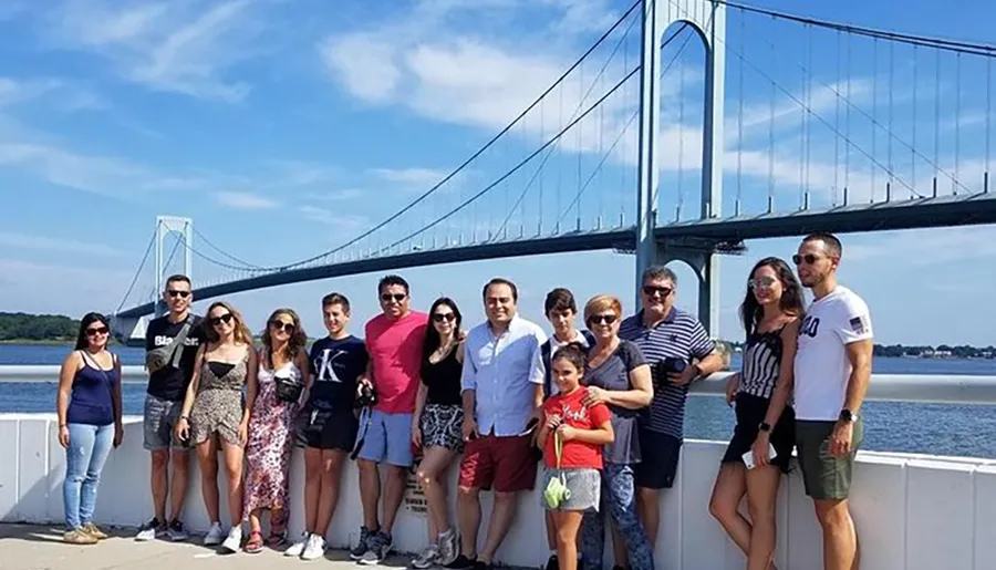 A group of people is posing for a photo in front of a large suspension bridge on a sunny day.