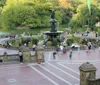 The image shows a lively scene of people gathering and walking around the Bethesda Terrace and Fountain in Central Park New York City on a sunny day