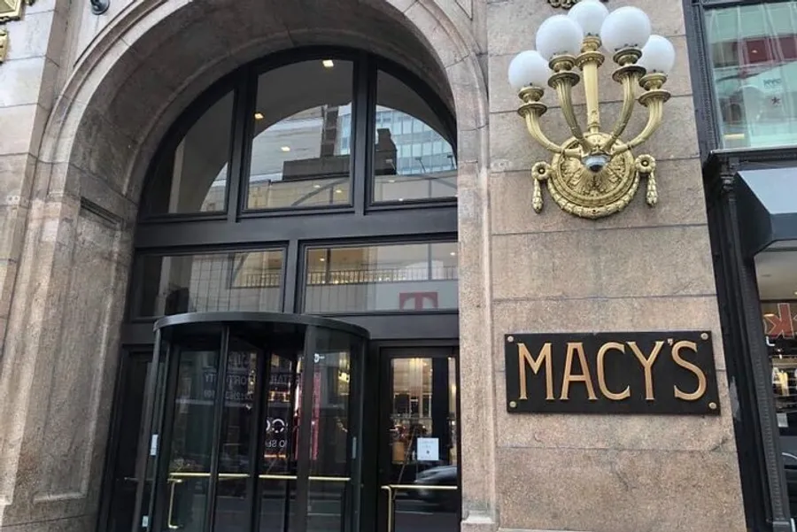 The image shows the exterior of a Macy's department store with a distinctive arch and gold-colored signage.