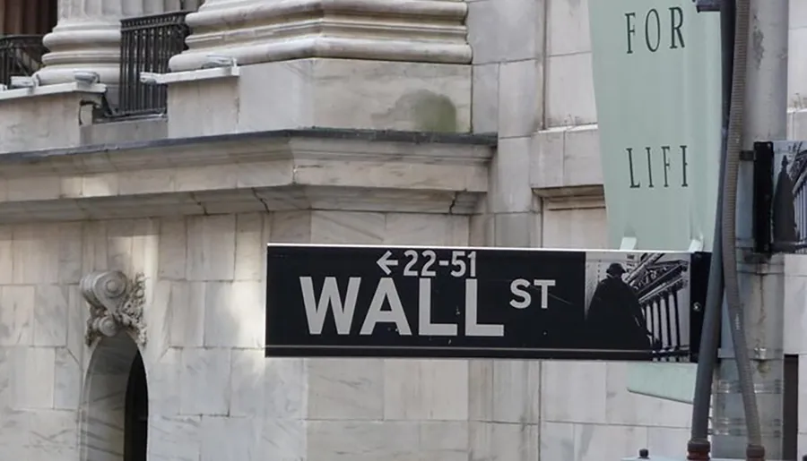 The image shows a directional sign for Wall Street with building numbers <22-51 against a background of a stone building with part of a banner reading FOR LI FI.