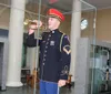 A person in a ceremonial military uniform is playing a trumpet in an indoor setting with exhibits in the background