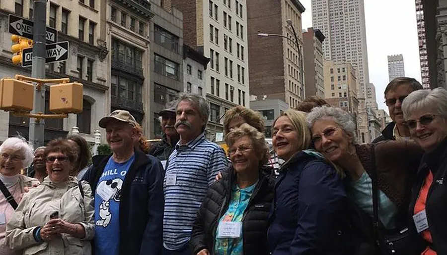 A group of smiling people, possibly tourists, gather closely together on a city street, with tall buildings in the background and a street sign overhead.