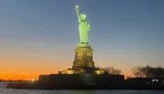 The Statue of Liberty is illuminated against a twilight sky showcasing a gradient from blue to warm orange.