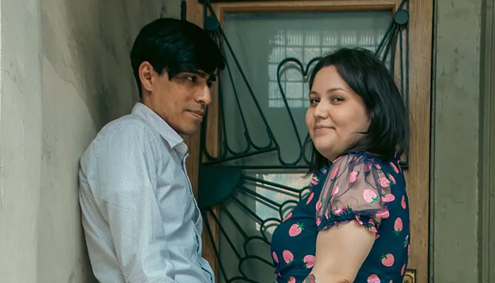 A man and a woman are standing in a doorway smiling towards the camera with a decorative ironwork feature beside them