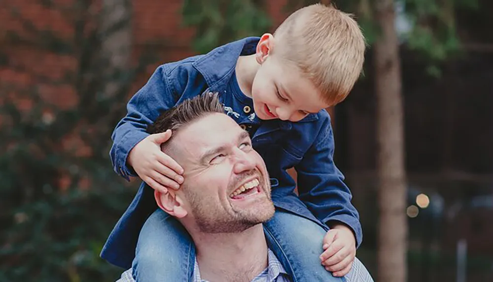 A joyful child sits on a mans shoulders both smiling and enjoying a playful and affectionate moment together