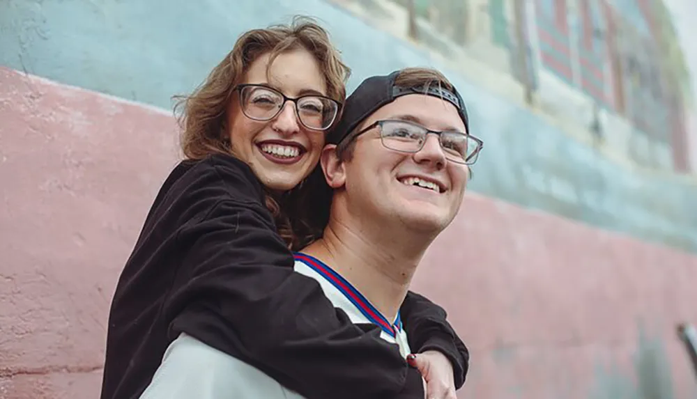 A joyful woman is hugging a smiling man from behind both appearing to be happy and enjoying the moment