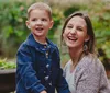 A young boy and a woman likely his mother are smiling joyfully in a garden setting