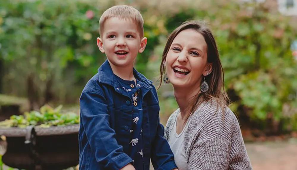 A young boy and a woman likely his mother are smiling joyfully in a garden setting