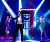 Two performers in sparkly cabaret-style costumes strike poses on a stage bathed in blue and white spotlight beams