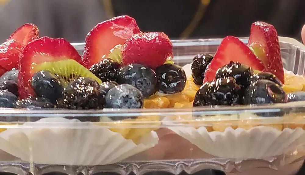 The image shows a colorful fruit tart with a variety of fresh berries and kiwi slices on top of a cream filling within a fluted pastry crust