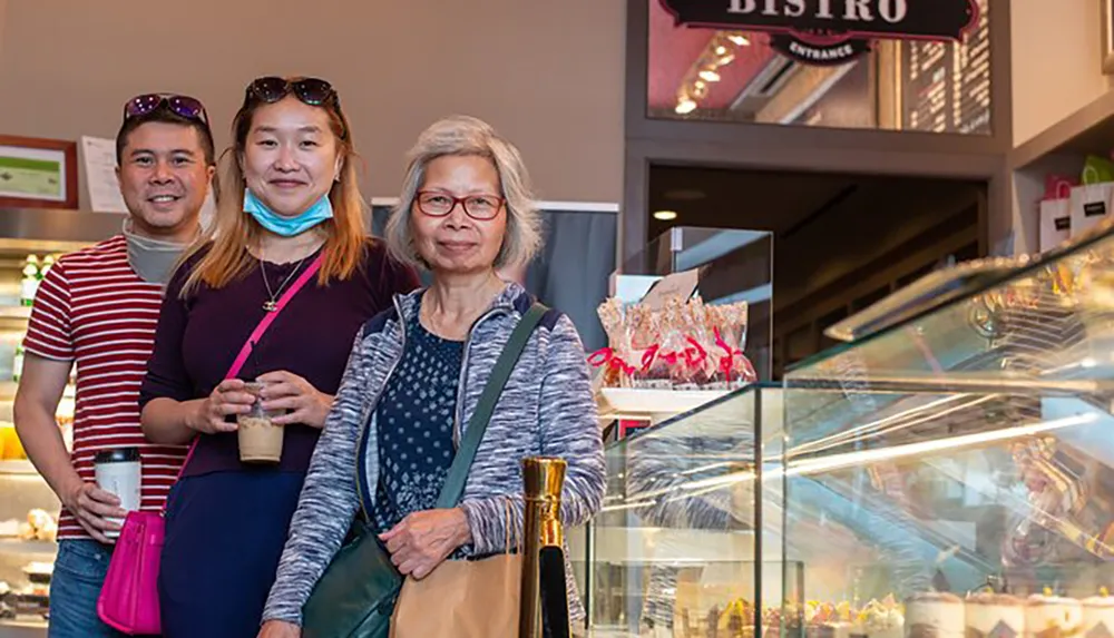 Three people are posing for a photo inside a cafe or bistro with one person wearing a face mask pulled down to their chin