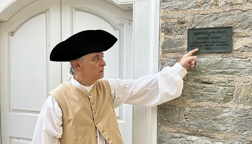 A person dressed in historical attire is pointing to a plaque on a stone wall
