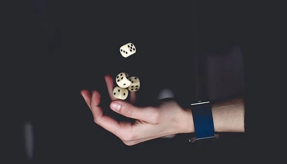 A persons hand is captured mid-motion tossing three white dice against a dark background