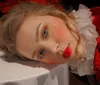 A person with glamorous makeup and a red costume with a frilly white collar is lying down gazing toward the camera